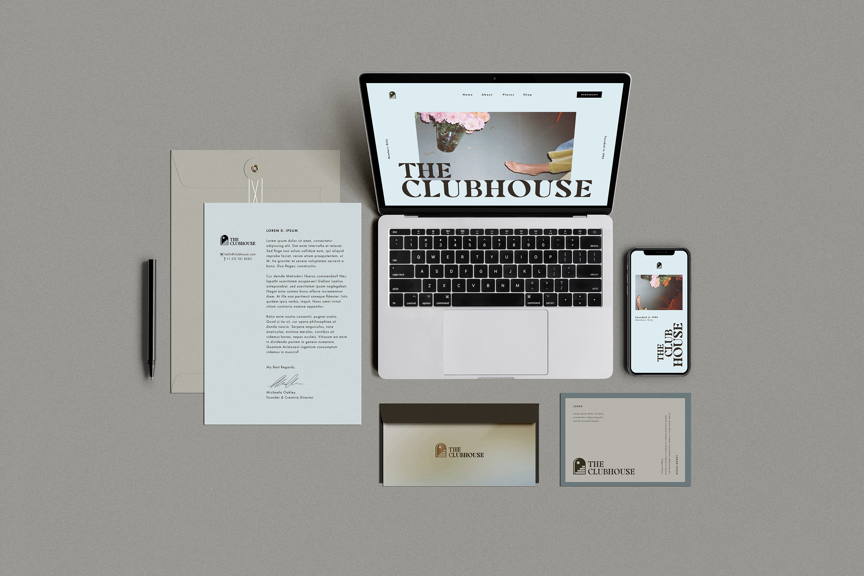 The Clubhouse stationary including an 8.5 inch by 11 inch letter & beige envelope, pen, Macbook & iPhone displaying The Clubhouse landing page, postcards and a dark brown envelope